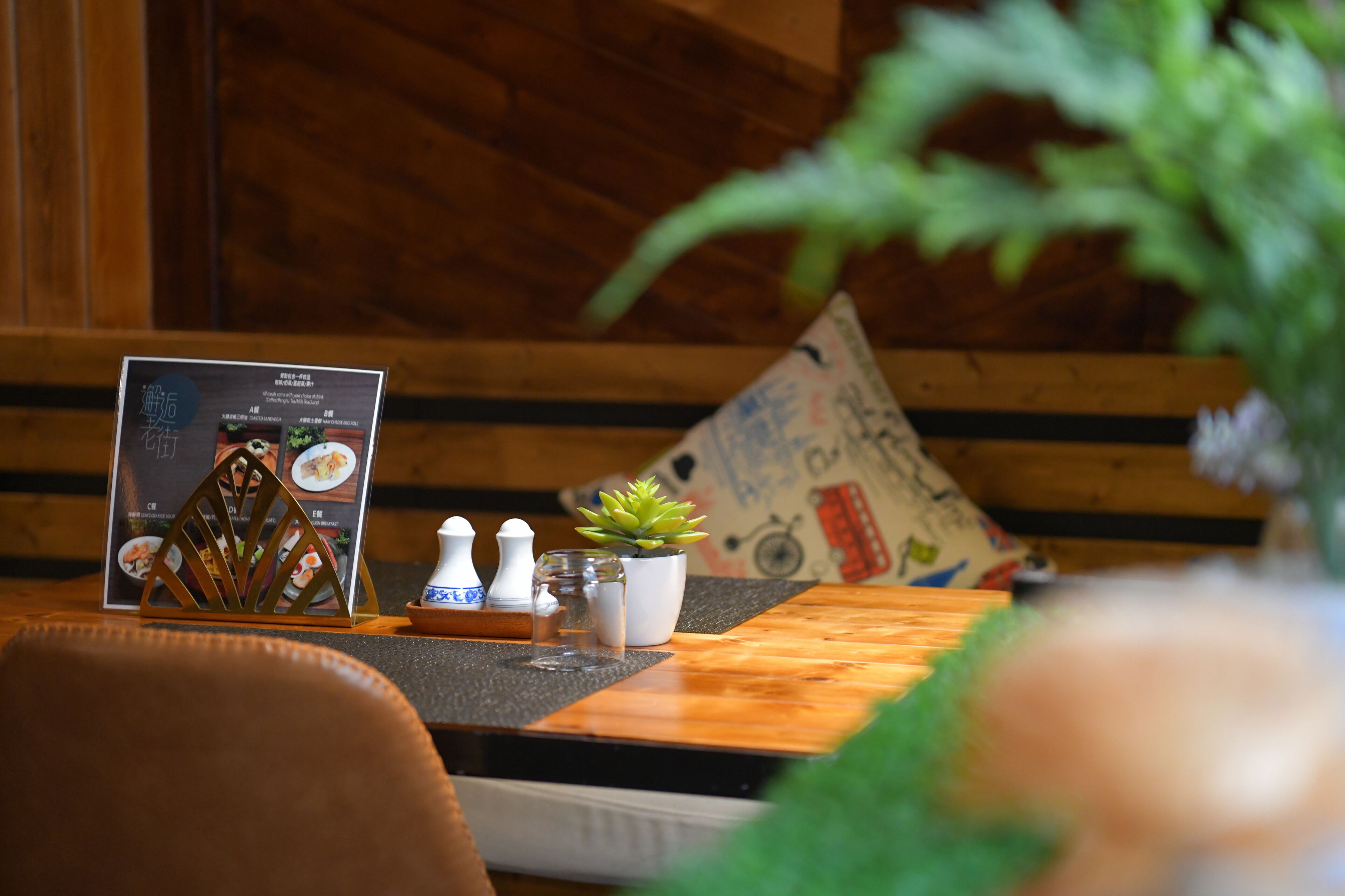 A wooden table with a menu stand, salt and pepper shakers, a small potted plant, and a decorative item.