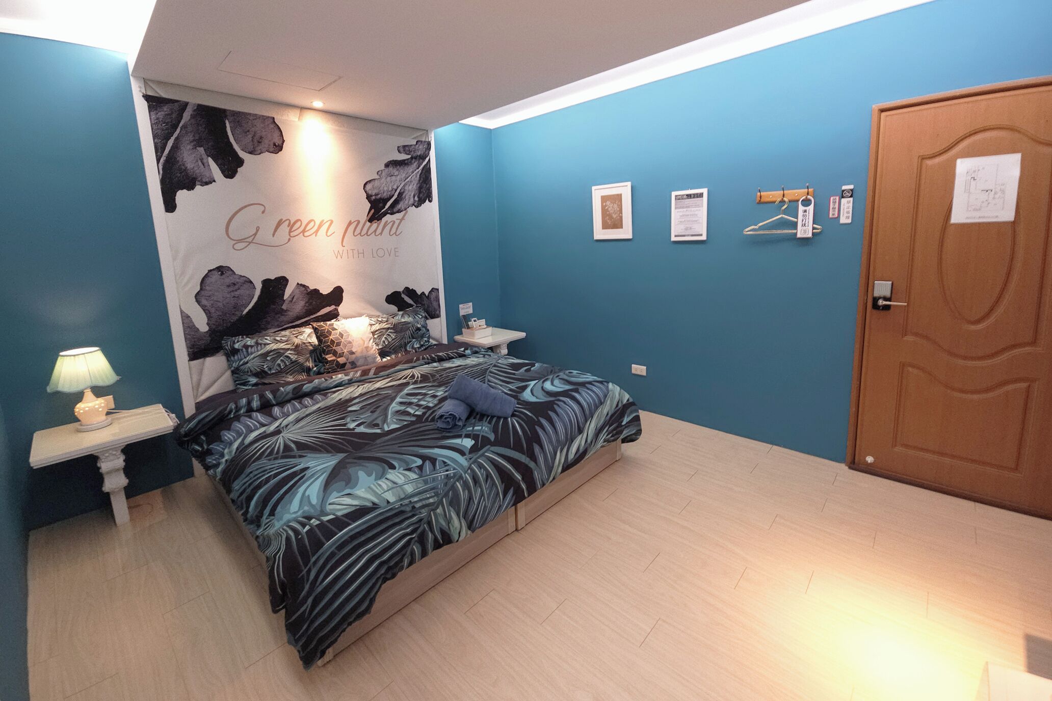 Une chambre à coucher avec un lit, une table de chevet, un mur orné d’une affiche et une porte.