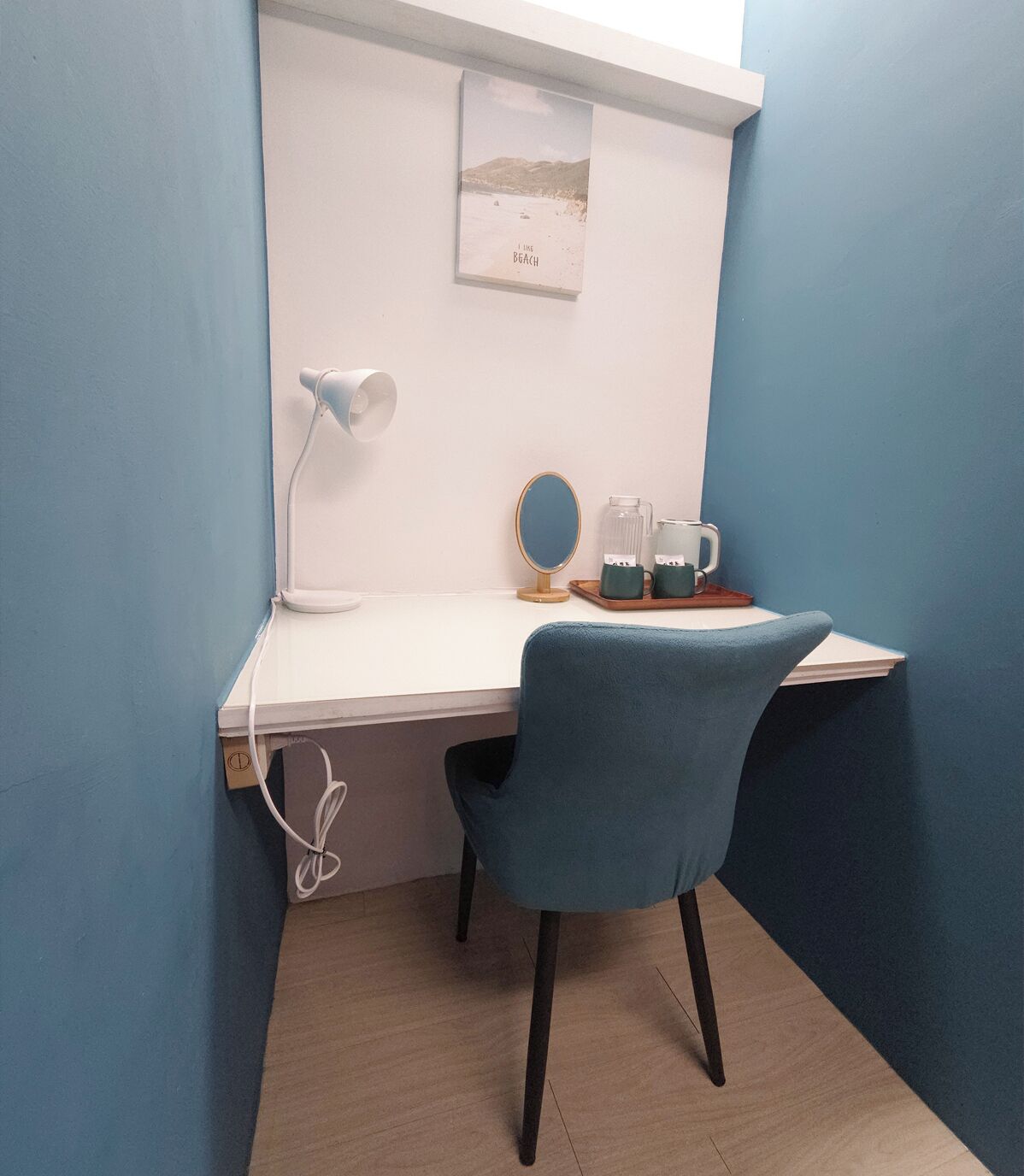 A corner workspace with a desk, chair, lamp, and a framed picture on the wall.