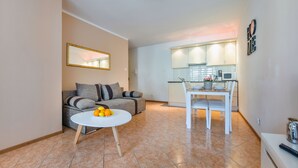 Una sala de estar moderna con un sofá, una mesa de comedor con un frutero, y una cocina al fondo.