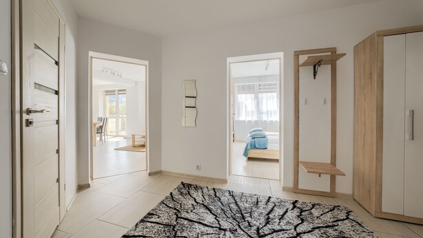 Un pasillo amplio con un rugado estampado, un armario de madera y una cama con ropa de cama azul en la habitación contigua.