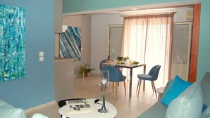 Una sala de estar moderna con un sofá, una mesa de comedor con sillas y una mesita de centro. Hay un cuadro en la pared y una planta sobre la mesa.