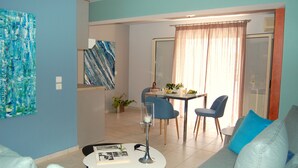 Una sala moderna con sofá, una mesa de comedor con sillas y una mesita de centro. Hay un cuadro en la pared y una planta en el suelo.