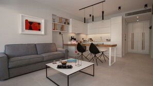 A modern living room with a grey sofa, a white coffee table, and black chairs. - Acropolis Golden Suites | 3 by GHH (Athina)