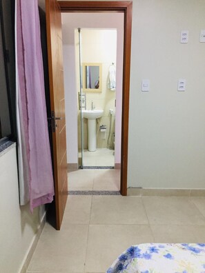 Une pièce avec un lit, une salle de bain visible à travers une porte ouverte, et une serviette rose accrochée à la porte.