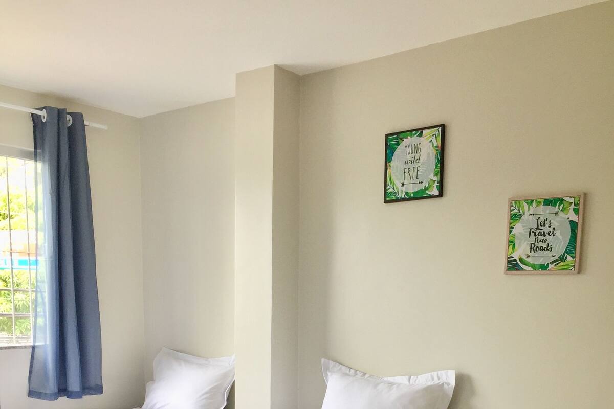 Ein Schlafzimmer mit zwei Einzelbetten, einem Fenster mit blauen Vorhängen und zwei gerahmten Motivationspostern an der Wand.