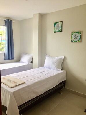 Une chambre avec deux lits simples, une fenêtre avec des rideaux bleus et deux affiches motivantes encadrées accrochées au mur.