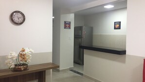Et reception område med et ur, et skilt der viser gratis WiFi, et køleskab og en reol med en bog.