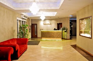 A hotel reception area with a red sofa, a reception desk, and a large window with a view. - Hotel Gniecki (Pruszcz Gdanski)