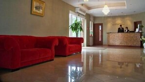 A hotel lobby with a red sofa, a reception desk, and a chandelier. - Hotel Gniecki (Pruszcz Gdanski)
