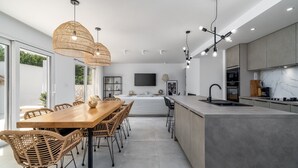 A modern kitchen with a central island, dining area with wicker chairs, and a large window providing natural light. - Villa Zen with private 32 sqm pool, summer kitchen, 7 km from the beach (Tugare)