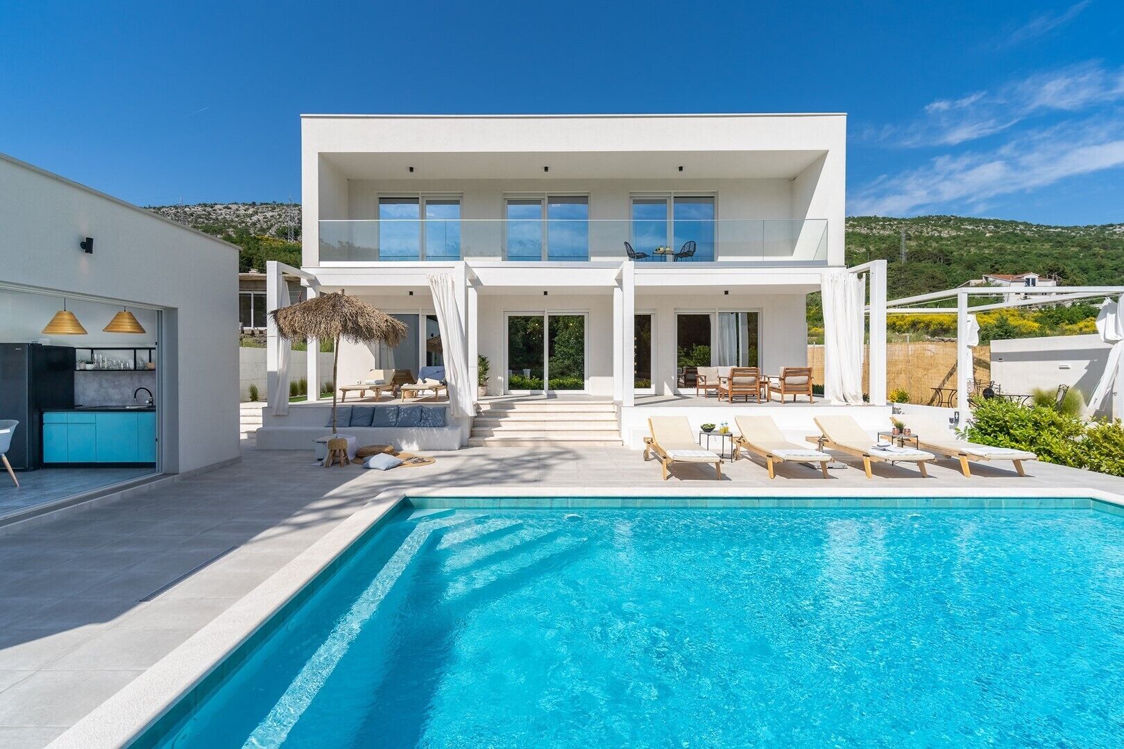 A modern two-story house with a swimming pool, outdoor seating, and a kitchen area.