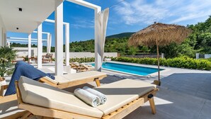 A poolside area with lounge chairs, a pool, and a thatched umbrella. - Villa Zen with private 32 sqm pool, summer kitchen, 7 km from the beach (Tugare)