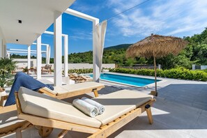 A poolside area with lounge chairs, a pool, and a thatched umbrella. - Villa Zen with private 32 sqm pool, summer kitchen, 7 km from the beach (Tugare)