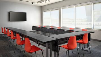 A conference room with a long table, red chairs, a flat-screen TV, and large windows.