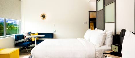 Quarto de hotel moderno com cama grande, uma secretária pequena, uma cadeira e janela com vista.