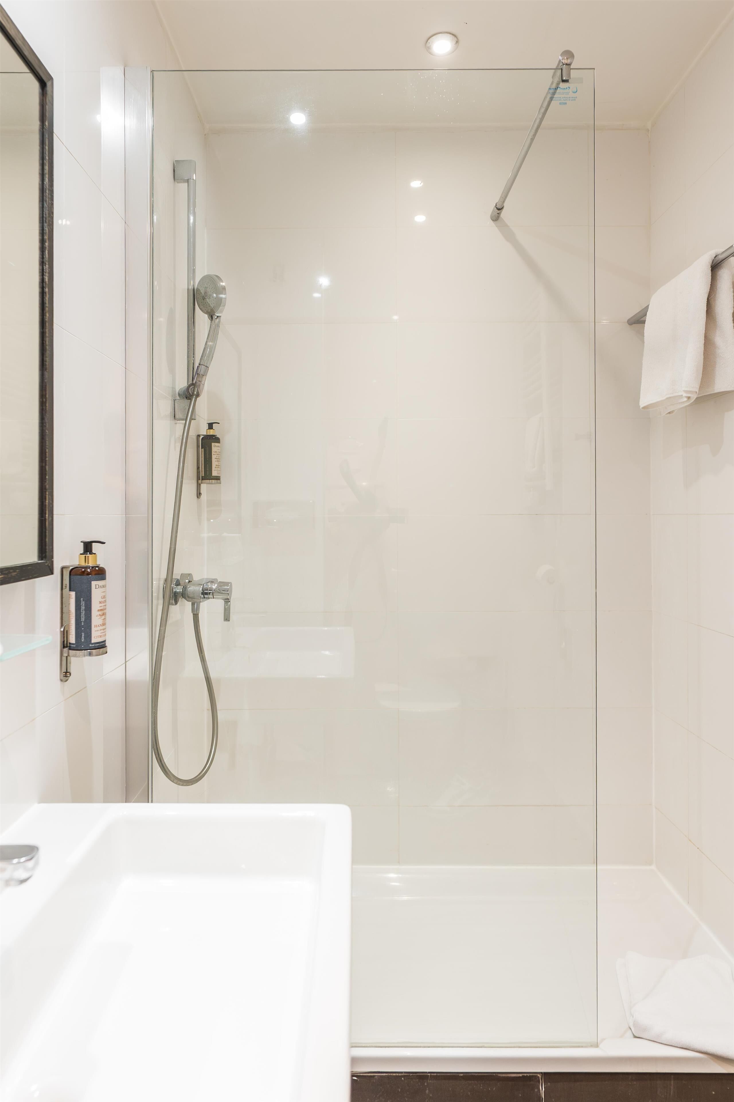 Un baño moderno con ducha de vidrio, lavamanos blanco y espejo.