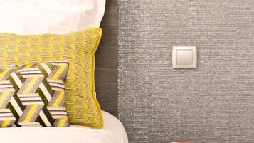 A modern bedroom with a bed, patterned pillows, a bedside table with a book, and a wall-mounted light fixture.
