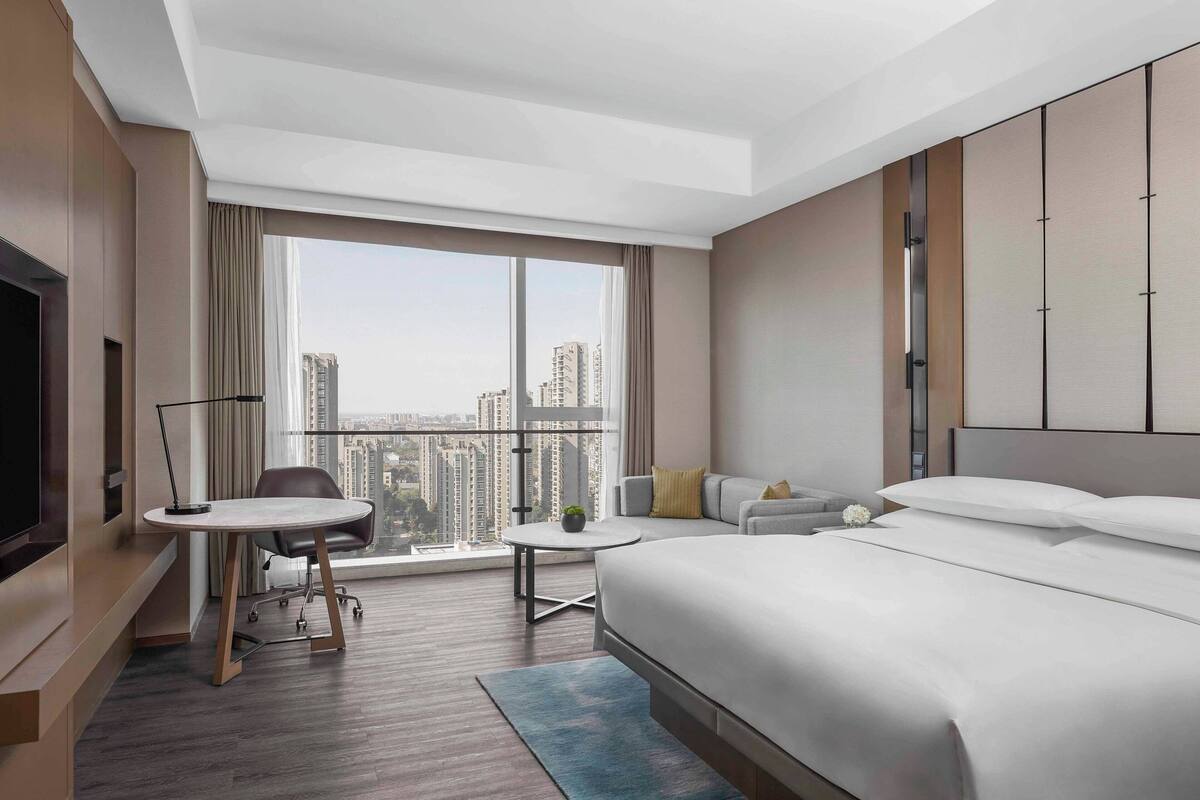 A modern hotel room with a large bed, a desk, a chair, and a TV.