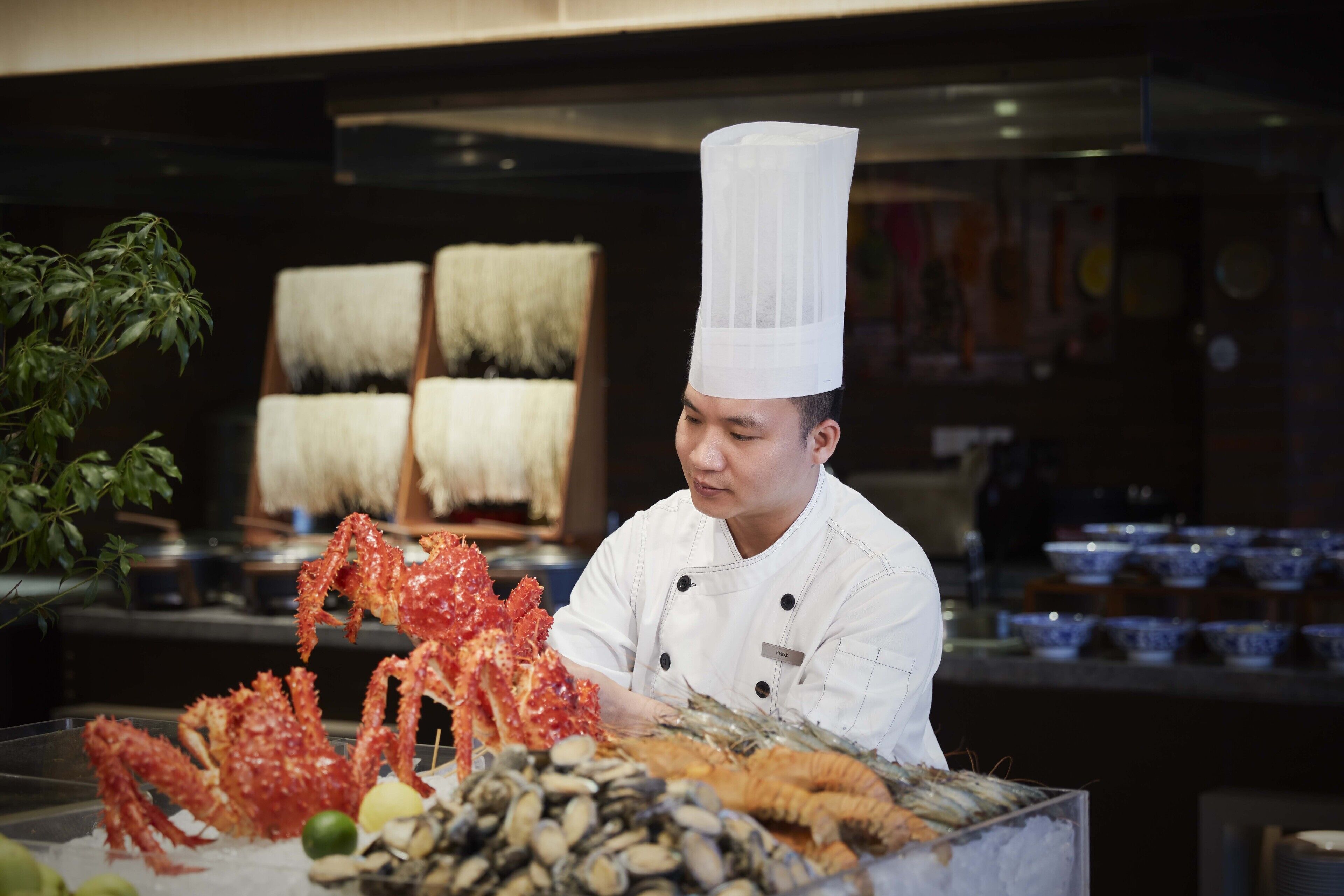 Un chef vêtu d'un uniforme blanc et coiffé d'un haut chapeau de chef, entouré de fruits de mer présentés sur un étal.