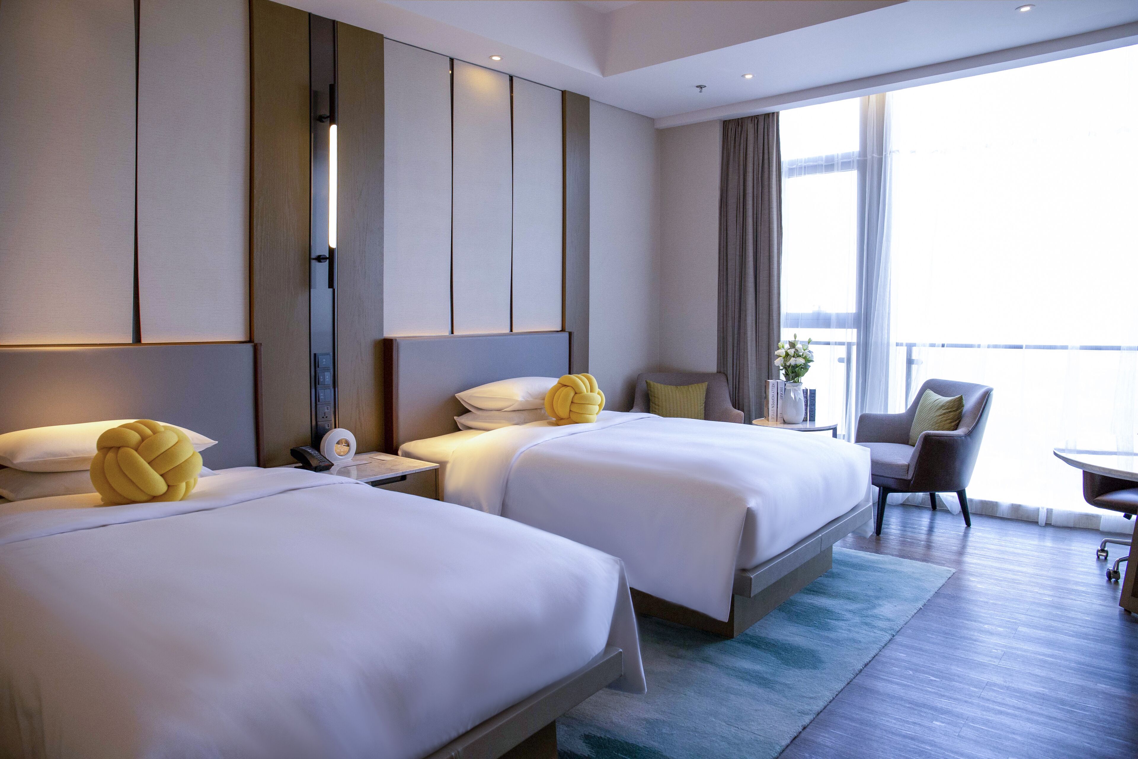 Een hotelkamer met twee bedden, een bureau, een stoel en uitzicht op buiten.