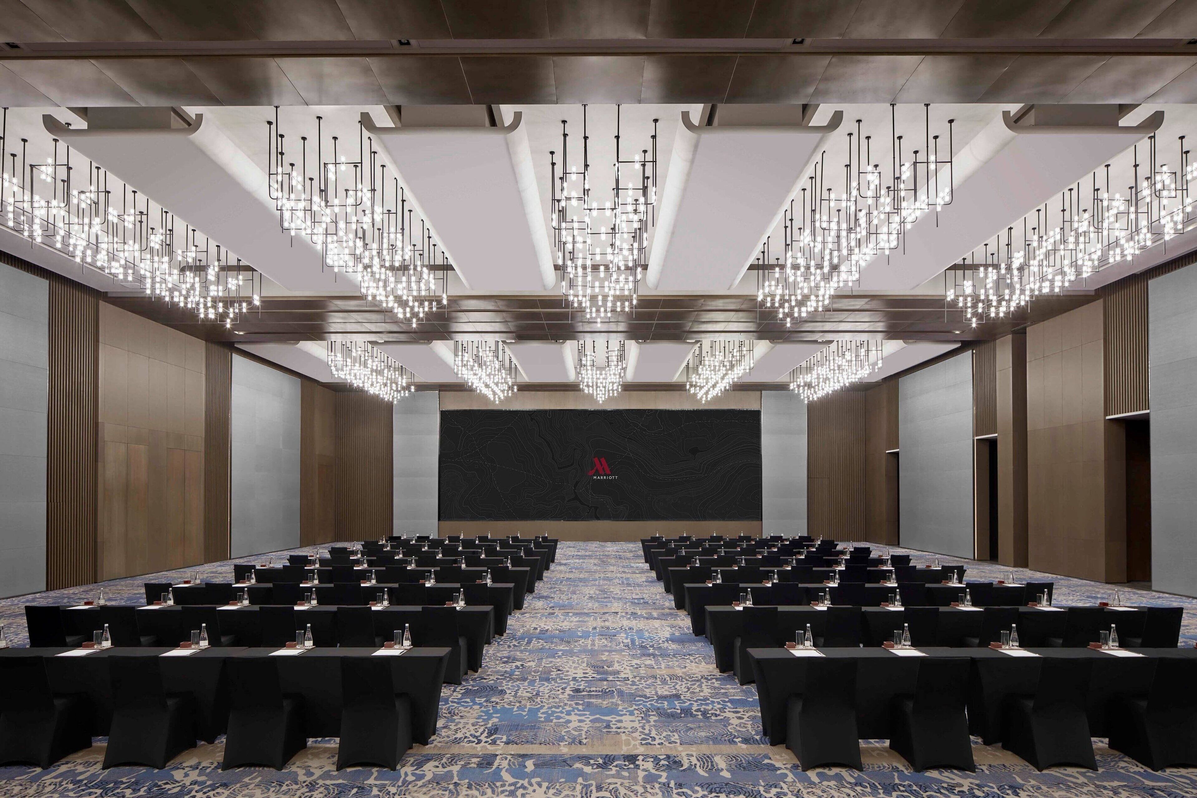 A conference room with rows of tables and chairs, a patterned carpet, and a large screen at the front.