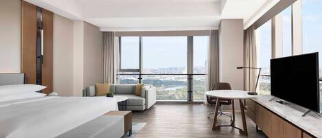A hotel room with a large bed, a sofa, a dining table, and a TV.