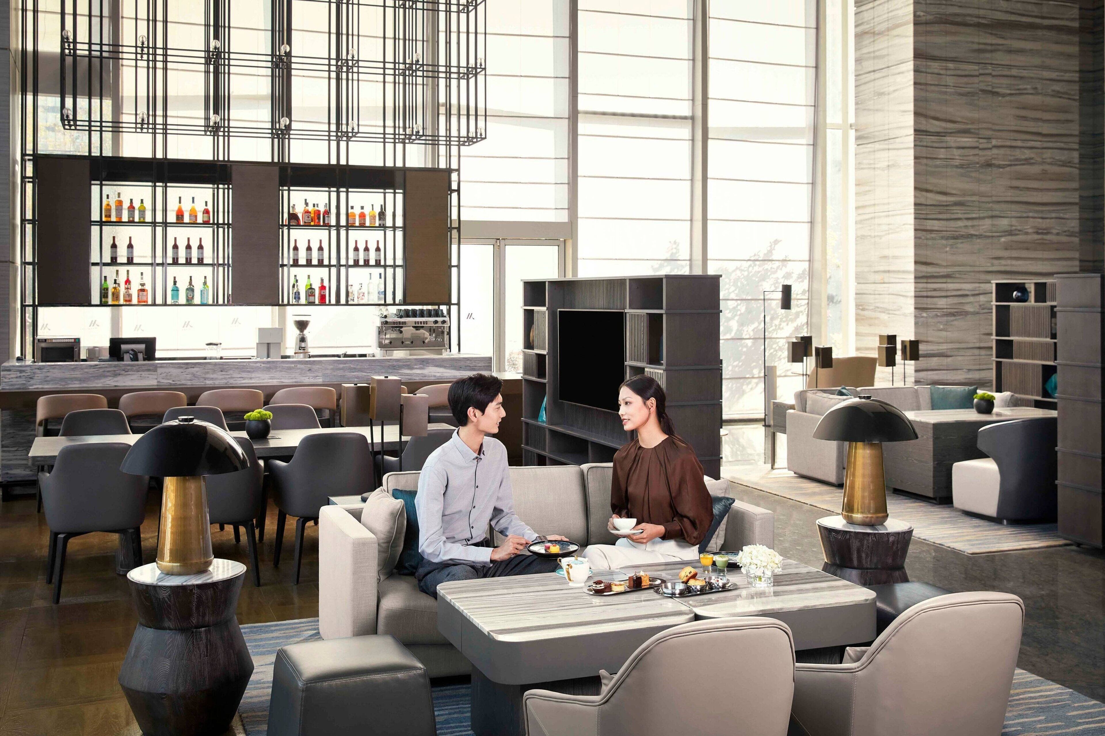 A modern hotel lobby with a bar area, seating arrangements, and a large window providing natural light.