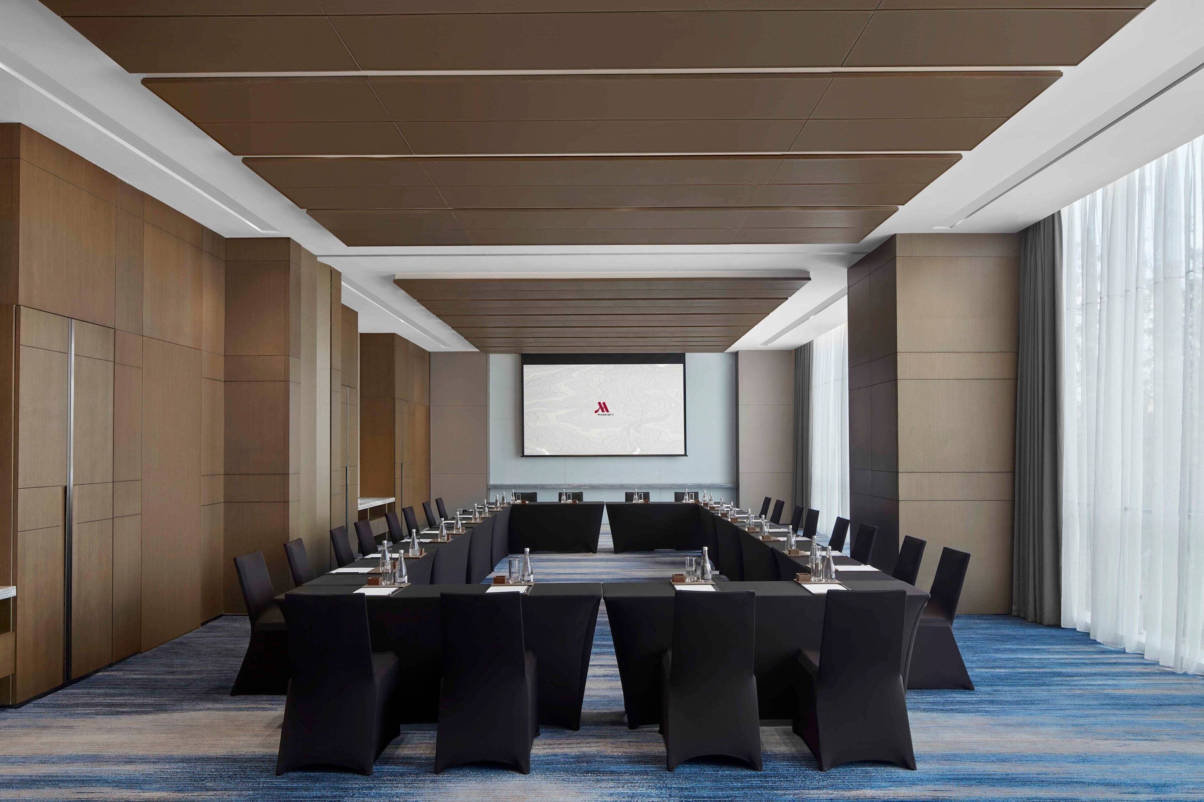 Un salón de conferencias con una larga mesa, sillas y una pantalla de proyector.