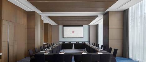 Un salón de conferencias con una larga mesa, sillas y una pantalla de proyector.