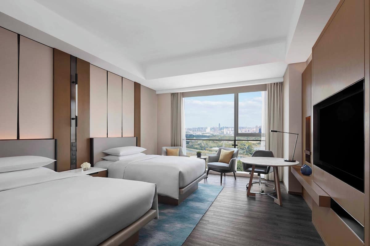 A hotel room with two beds, a desk, a chair, and a TV.
