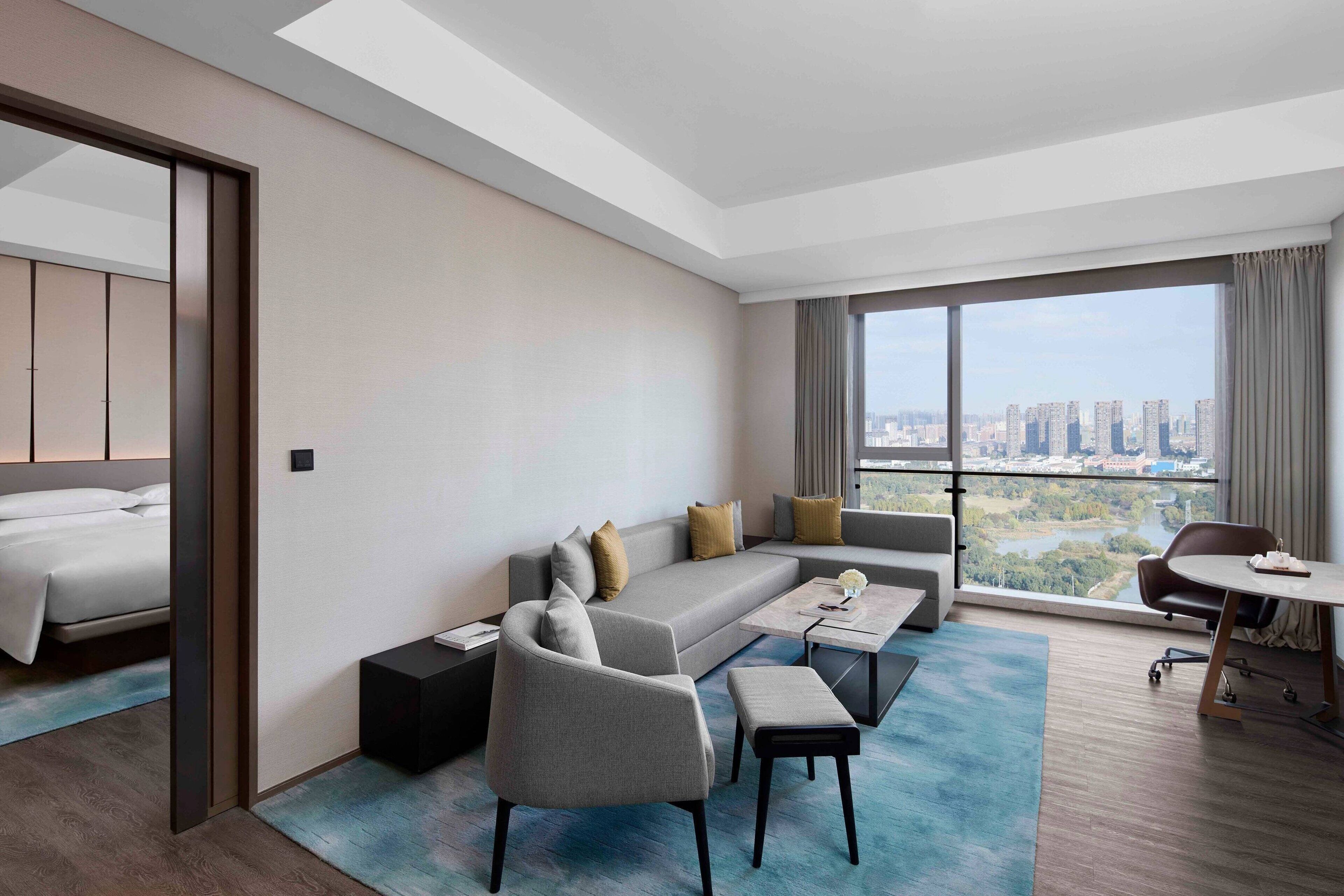 Een moderne hotelkamer met een groot bed, een slaapbank, een salontafel en een eethoek met uitzicht op de stad.