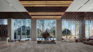 Un vestíbulo amplio con diseño moderno, que cuenta con un amplio espacio de descanso, una escultura geométrica única y grandes ventanales con vistas al exterior.