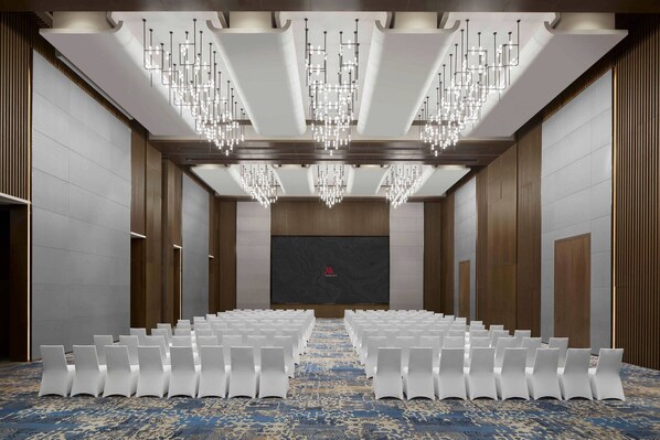 A conference room with rows of white chairs, a patterned carpet, and a large screen at the front.