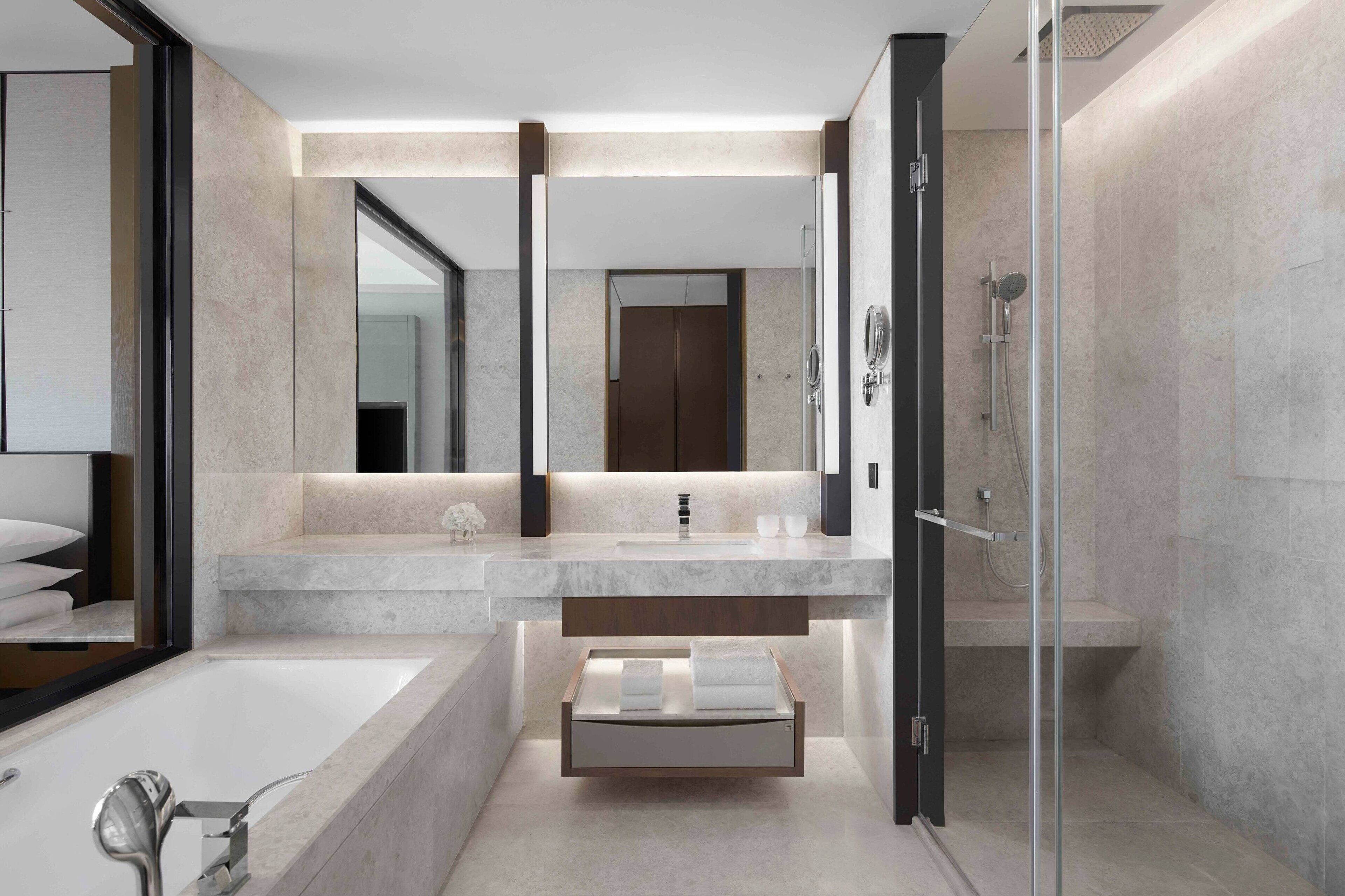 A modern bathroom with a large mirror, a bathtub, a shower, and a vanity with a countertop.
