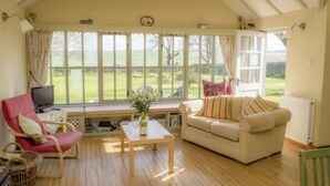A cozy living room with a red chair, a beige sofa, a wooden coffee table, and a television. - 2 bedroom cottage, with far reaching views of the garden and open countryside. (Whitehills)