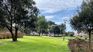 Ein Park mit einer Rasenfläche, Bäumen, einem Spielplatz und einem Gebäude im Hintergrund.