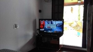 Ein Zimmer mit einem Bett, einem Fernseher, einem Ventilator und einer Tür, die nach draußen führt.