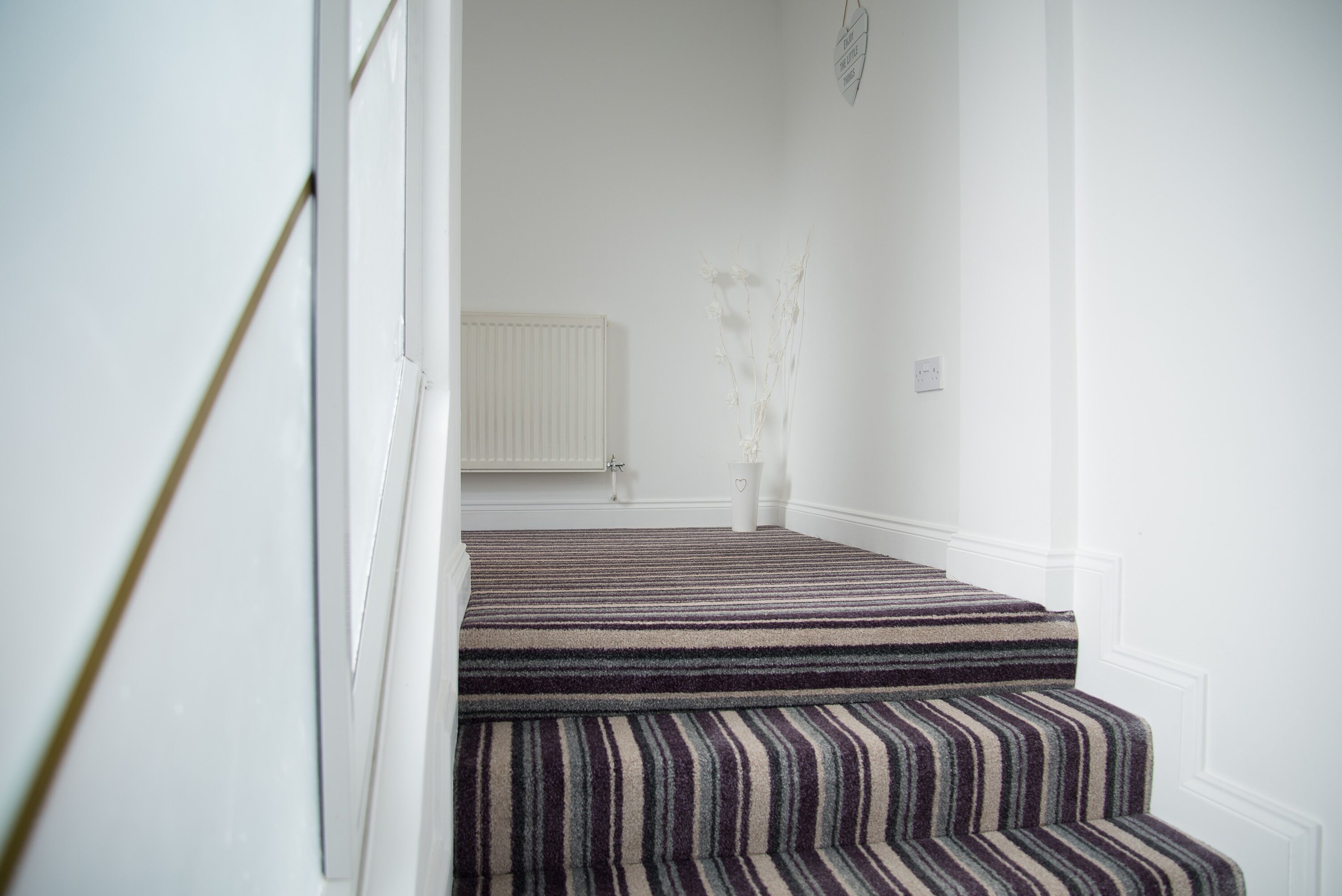 A staircase with striped carpet leading to a landing.
