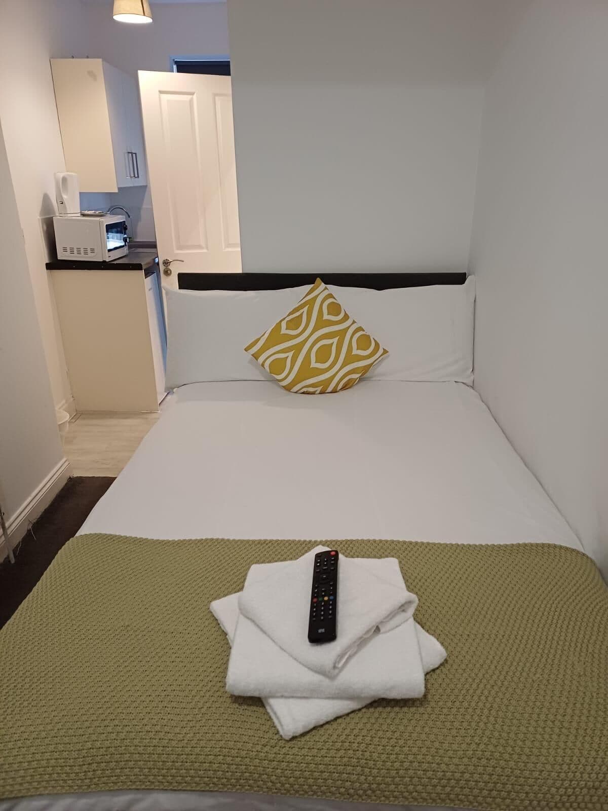 A hotel room with a bed, a remote control, a microwave, and a door to the bathroom.