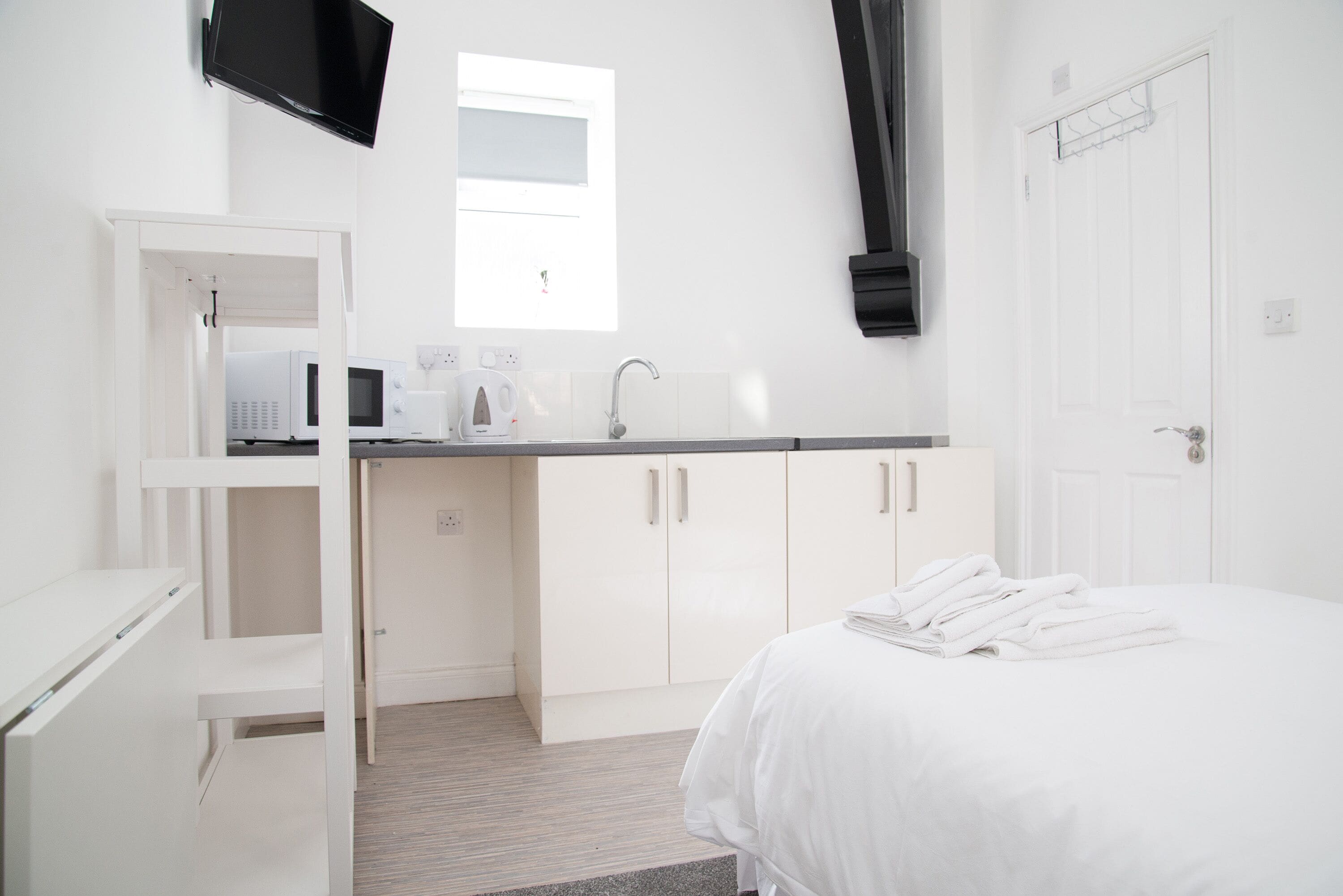 A modern hotel room with a bed, a kitchenette with a microwave, a coffee maker, and a flat-screen TV.
