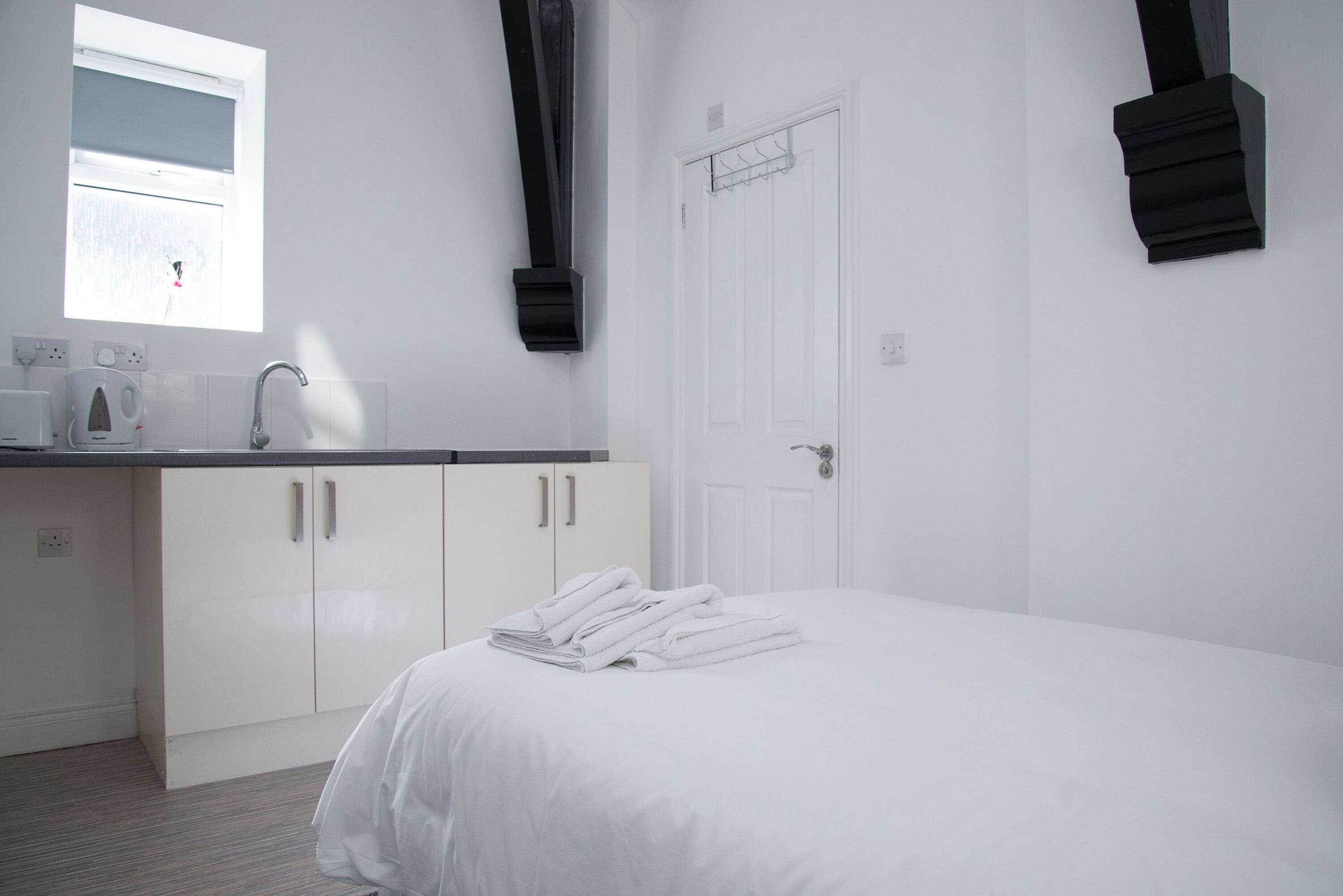 A clean, modern hotel room with a bed, a small kitchenette, a window, and a door.