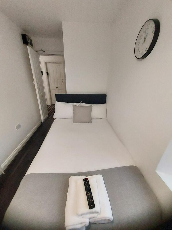 Una habitación de hotel con una cama, un reloj en la pared y un control remoto sobre la cama.