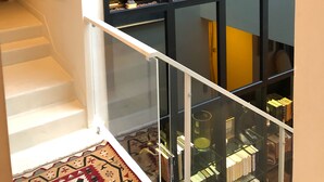 Un interior moderno con una escalera que baja a un nivel inferior, barandilla de vidrio y una colección de esculturas en estanterías.