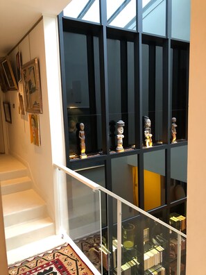 Ein modernes Interieur mit einer Treppe, die in eine untere Ebene führt, einem Glasgeländer und einer Sammlung von Skulpturen auf Regalen.