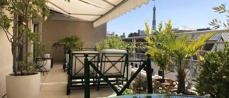 Terraço no telhado com plantas em vasos, móveis de exterior e vista para uma torre ao fundo.