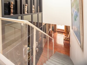 A staircase with a glass railing leading to a room with a wooden floor, a painting on the wall, and a chair.