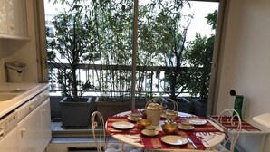 Un comedor con una mesa dispuesta para cuatro personas, rodeada de sillas de metal blanco. Una ventana ofrece vistas a árboles y edificios.