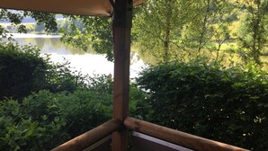 A wooden balcony with a view of a lake surrounded by lush greenery. - Camping de Matour (Matour)