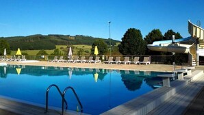 A swimming pool with lounge chairs and umbrellas, surrounded by a wooden deck and a view of green hills. - Camping de Matour (Matour)